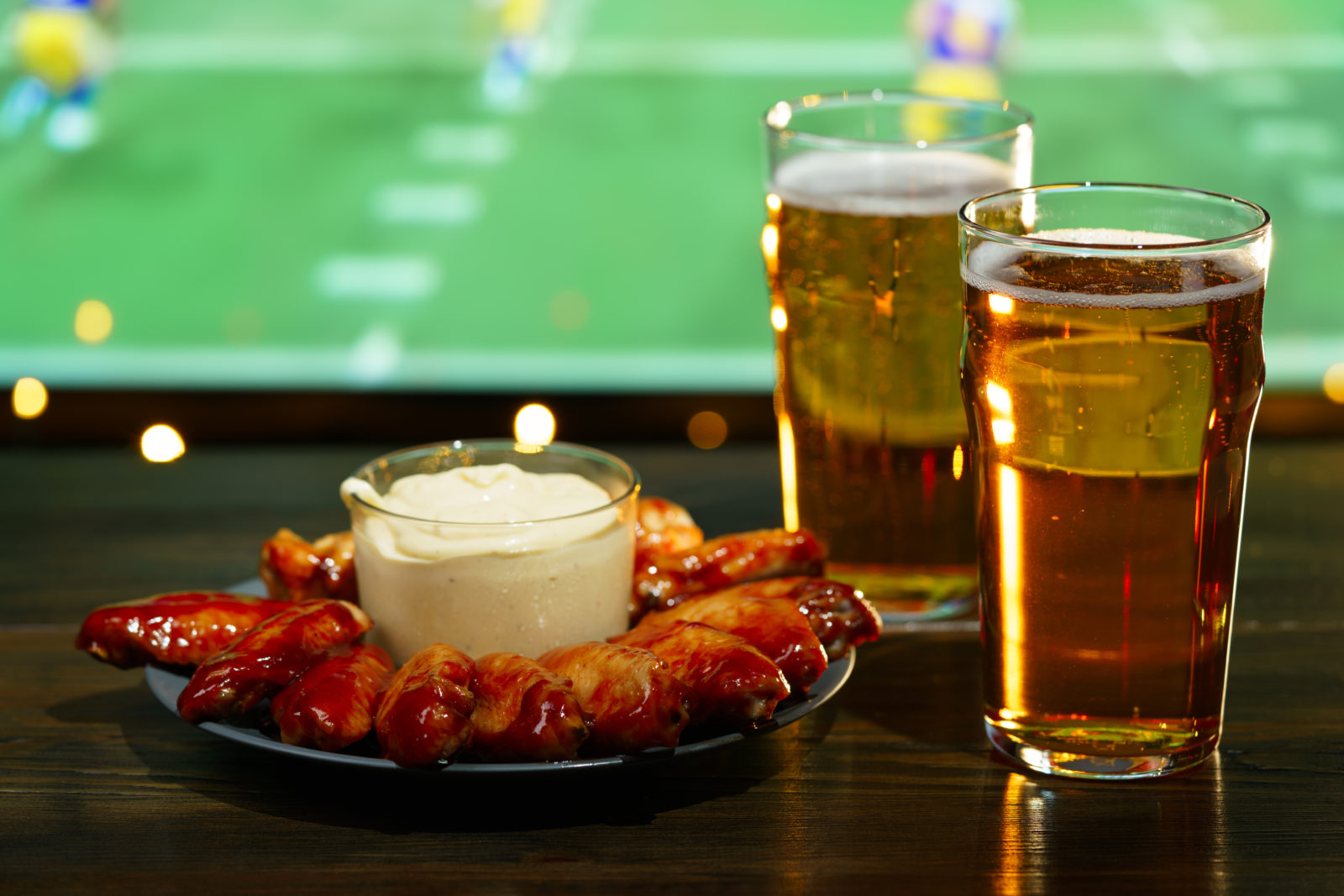 Hot barbecue chicken wings with 2 beer glasses on a dark wooden table served with honey mustard sauce. Football on a background, high resolution 2023/02/AdobeStock_251013213.jpeg 