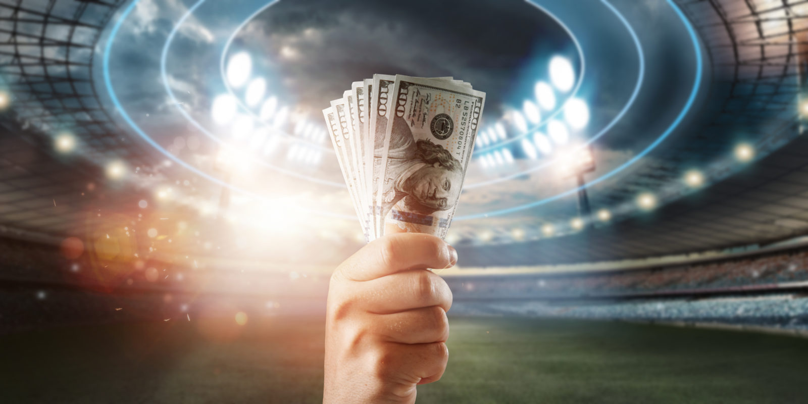 Close-up of a man's hand holding US dollars against the background of the stadium. The concept of sports betting, making a profit from betting, gambling. American football 2023/02/AdobeStock_408077810.jpeg 