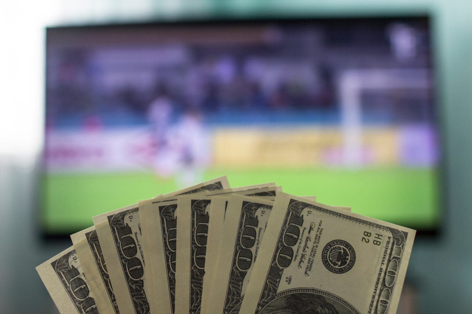 Men's hands keep money dollars against the background of a TV set on which football is playing, close-ups, gain 2023/03/AdobeStock_208490250.jpeg 