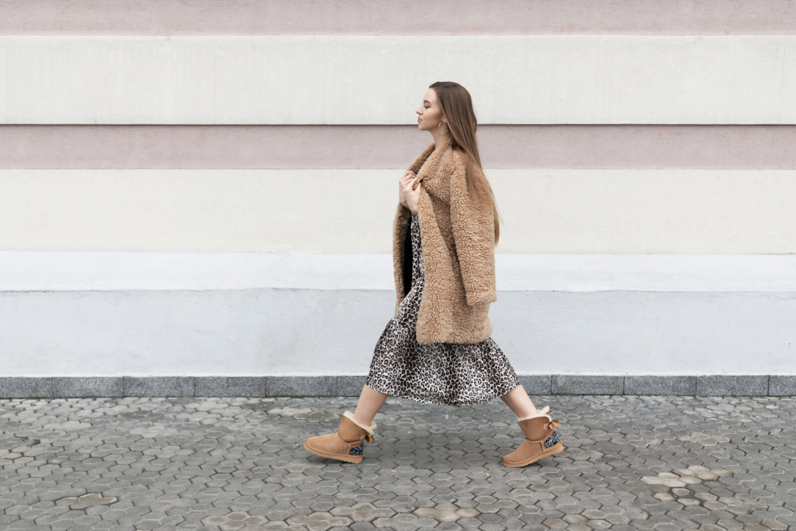 artificial fur coat, long leopard print dress, ugg boots, a small shoulder bag, a beautiful white model girl with long hair poses cheerfully walks on the street near the wall 2024/02/AdobeStock_304119895.jpeg 