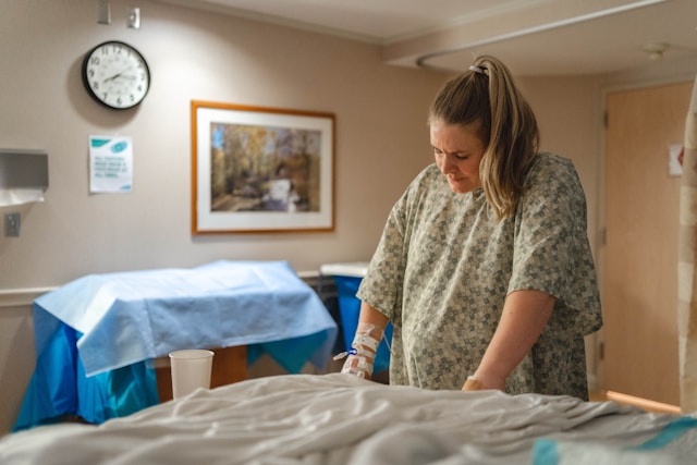 Pregnant woman in hospital gown leaning against bed