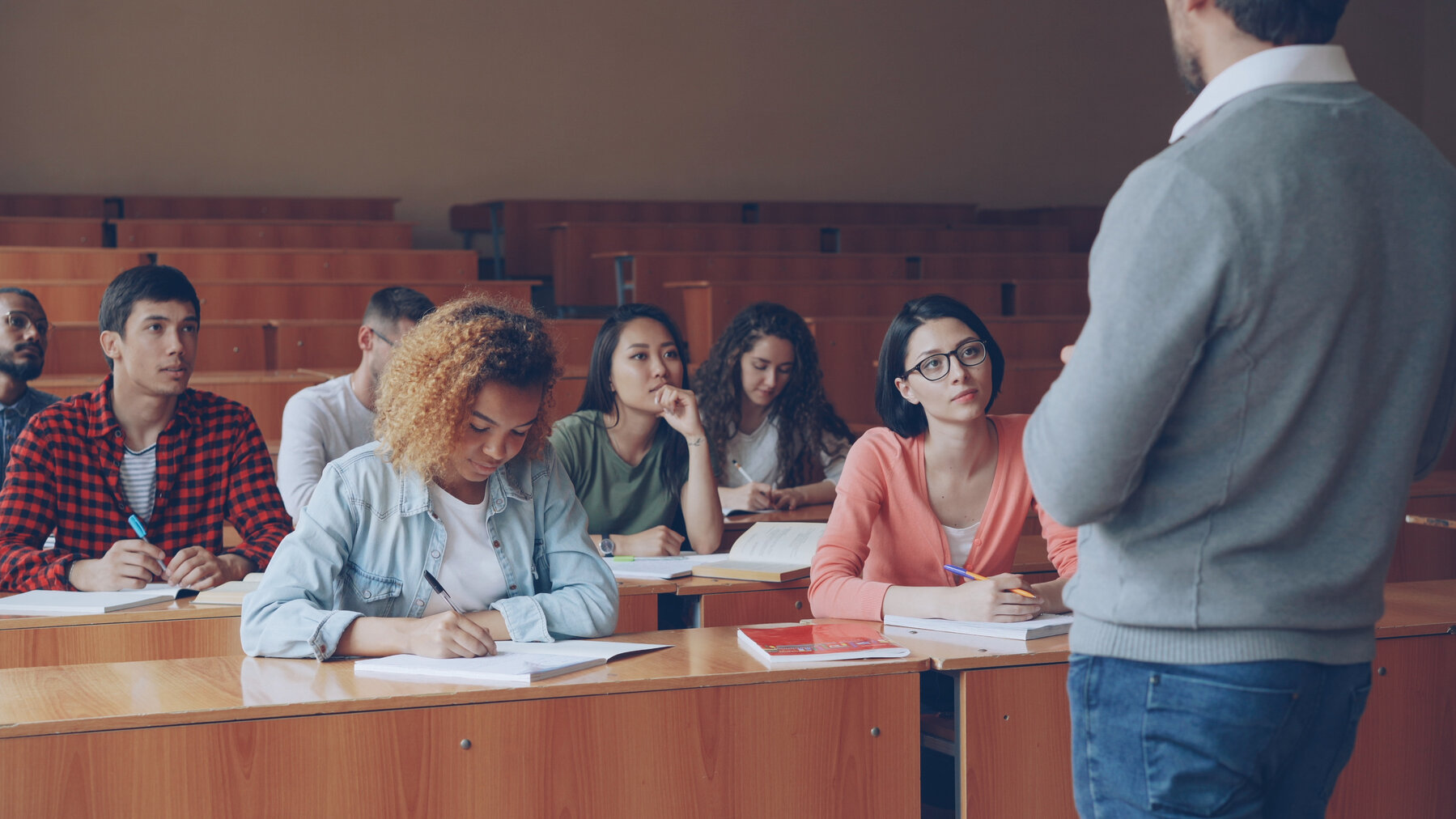 Emotional tutor is speaking to adult students explaining new information while attentive pupils are listening and taking notes. Profession, education and people concept.